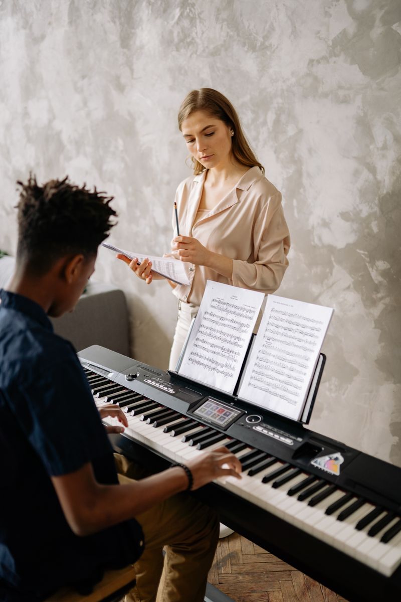 A young student receiving piano lessons from a teacher, focusing on music sheets.