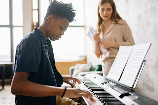 A teenage boy practicing piano during a music lesson with a teacher nearby.