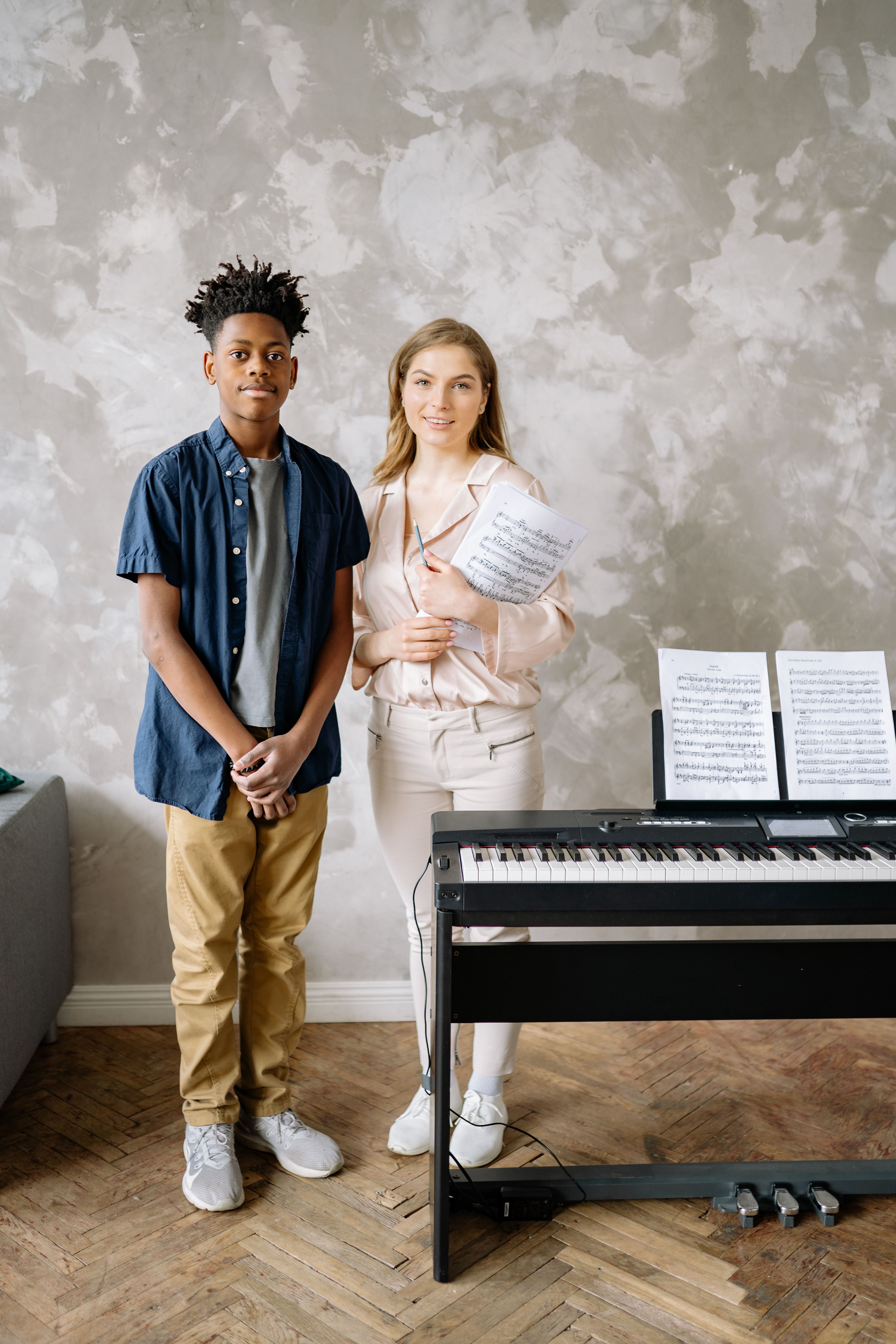 A teacher and teenage student with sheet music beside the piano