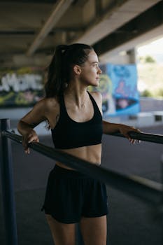 Young woman in sportswear stretching under an overpass with graffiti, emphasizing fitness and urban lifestyle.