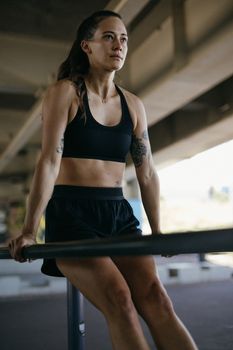 A strong woman in athletic wear performs exercises on outdoor parallel bars, showcasing fitness and determination.
