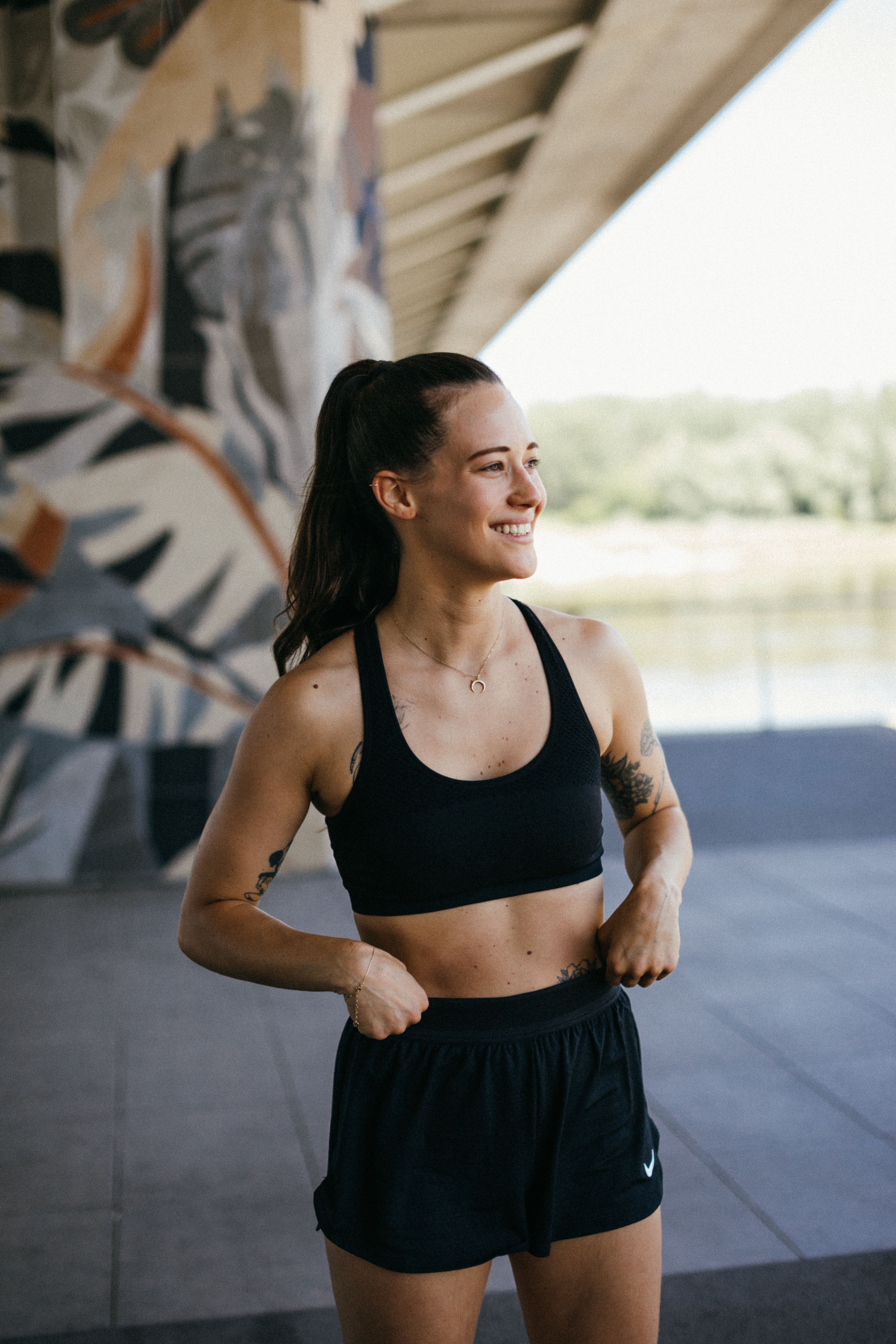 A woman in active wear smiling confidently outdoors under a bridge.