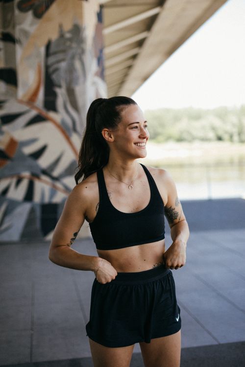 Free A woman in active wear smiling confidently outdoors under a bridge. Stock Photo