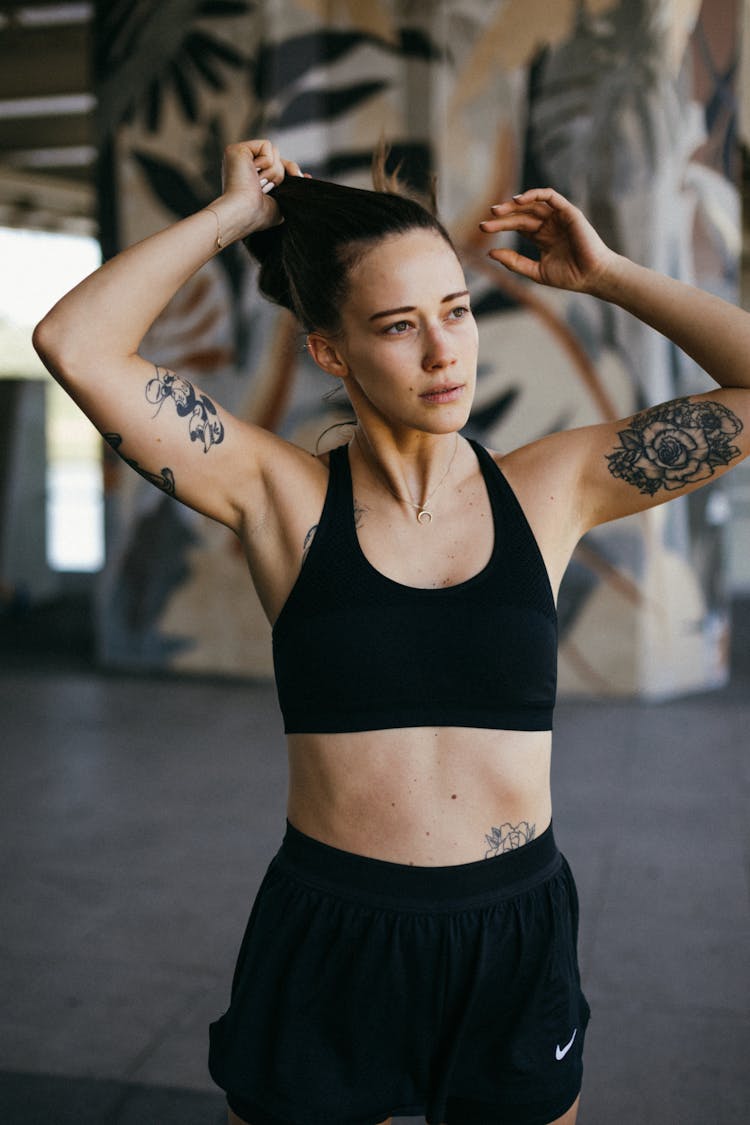 A Tattooed Woman In Black Sports Bra Holding Her Hair