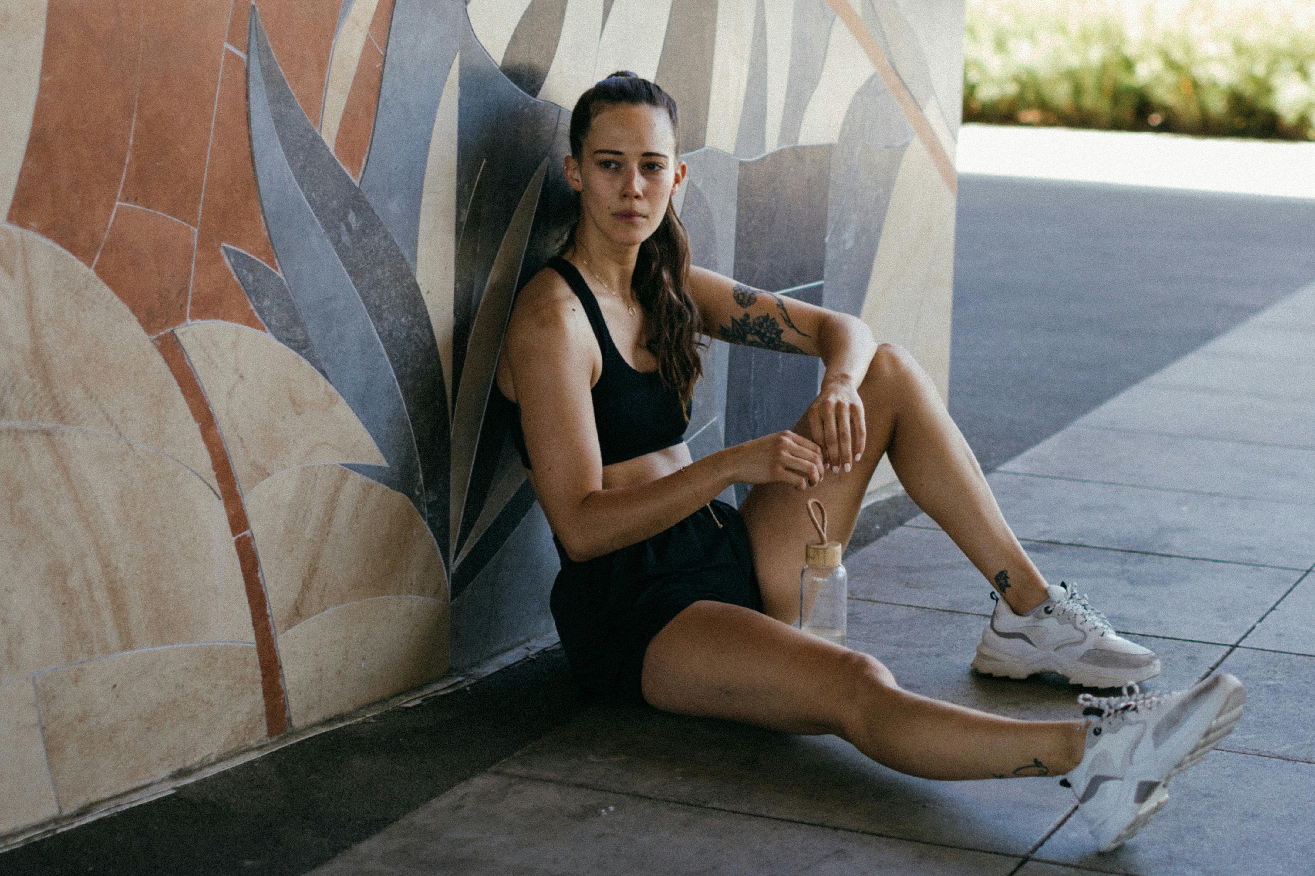 A young woman taking a break outdoors, sitting by a mural, looking relaxed yet thoughtful.