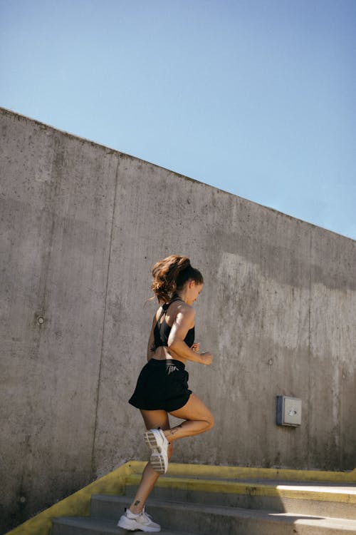 Free Woman in Black Tank Top and Black Shorts Running on Concrete Steps Stock Photo