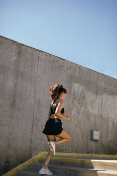 Athletic young woman in activewear running on outdoor concrete stairs, showcasing fitness and strength.