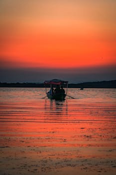 A serene boat silhouette against a vibrant sunset sky reflecting on a still lake.