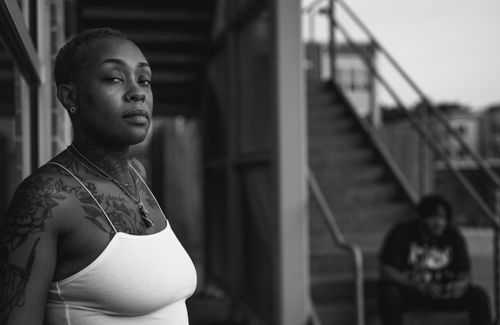 Free Striking black and white portrait of a tattooed woman in a spaghetti strap top standing outdoors. Stock Photo