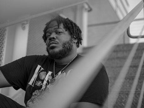 Monochrome portrait of a man with dreadlocks sitting on stairs, creating an introspective mood.