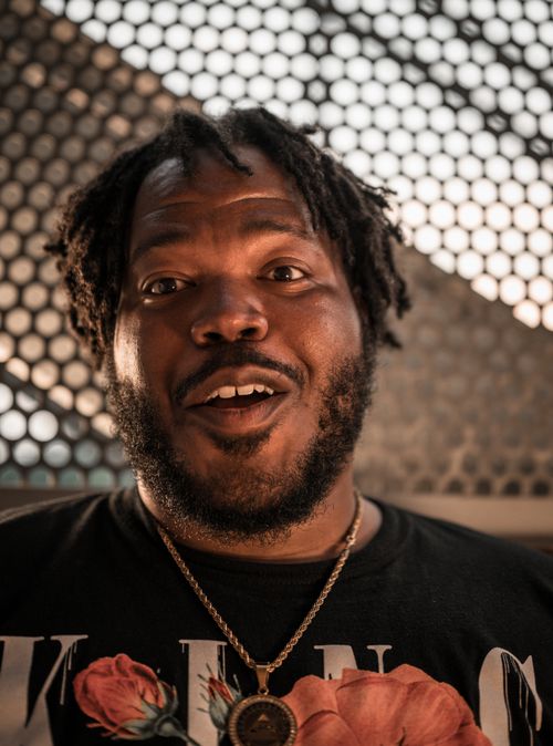 Free Smiling man with dreadlocks wearing a necklace against a geometric background. Stock Photo