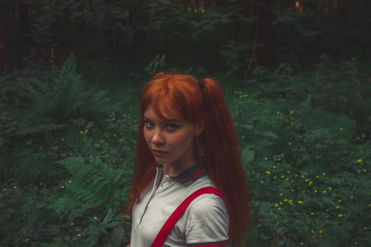 Portrait of a young redhead woman standing in a vibrant, green forest background.