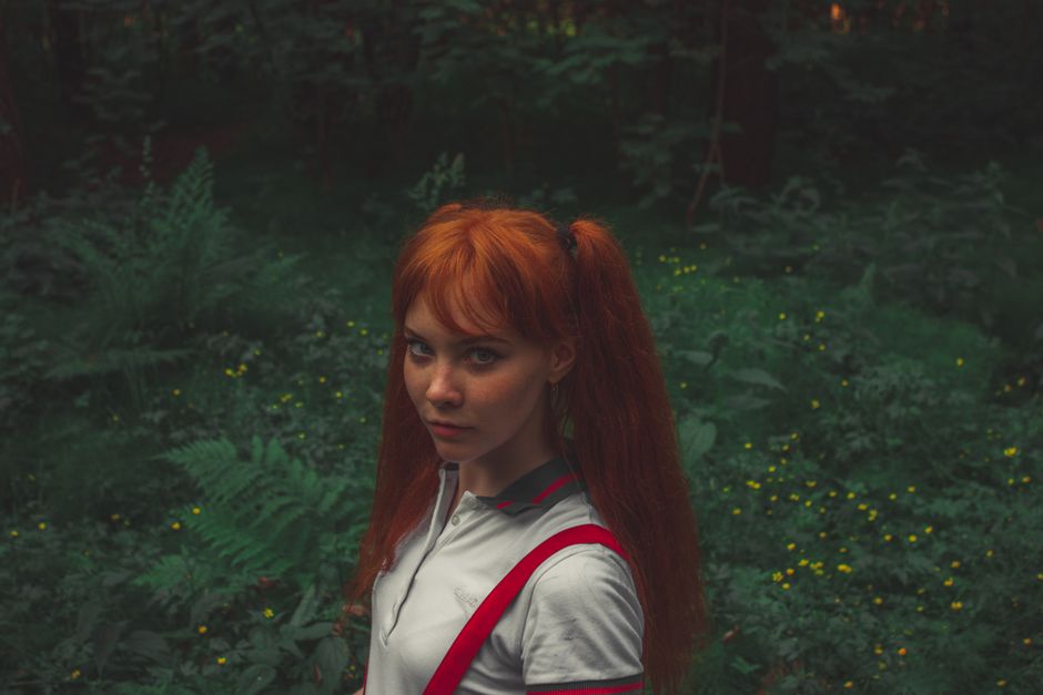 Portrait of a young redhead woman standing in a vibrant, green forest background.