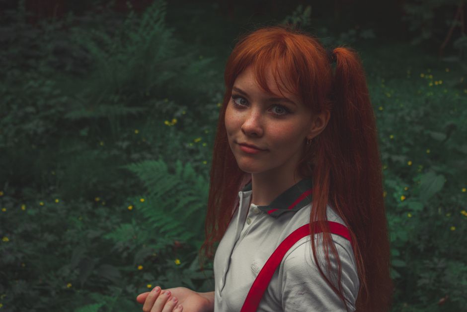 Portrait of a young woman with red hair outdoors in a green setting.