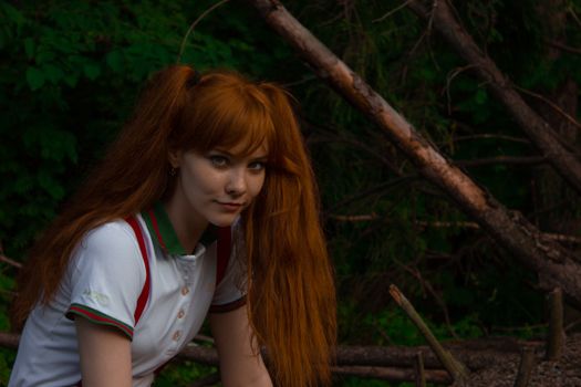 Portrait of a woman with red hair in a wooded outdoor setting.