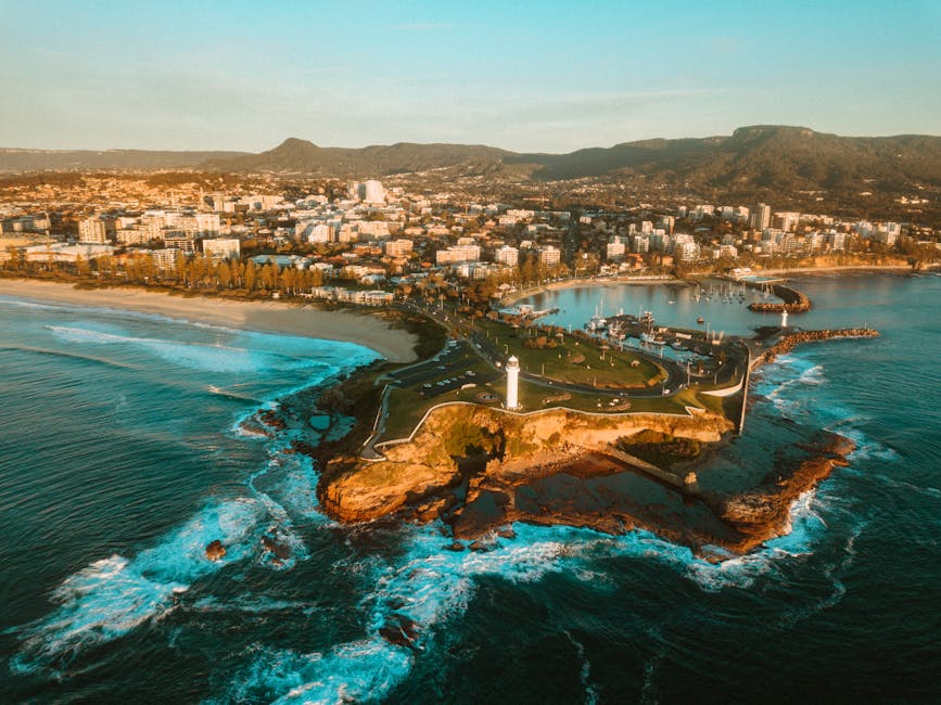 A breathtaking aerial view of a city coastline with a prominent lighthouse and surrounding sea, shot during the day.