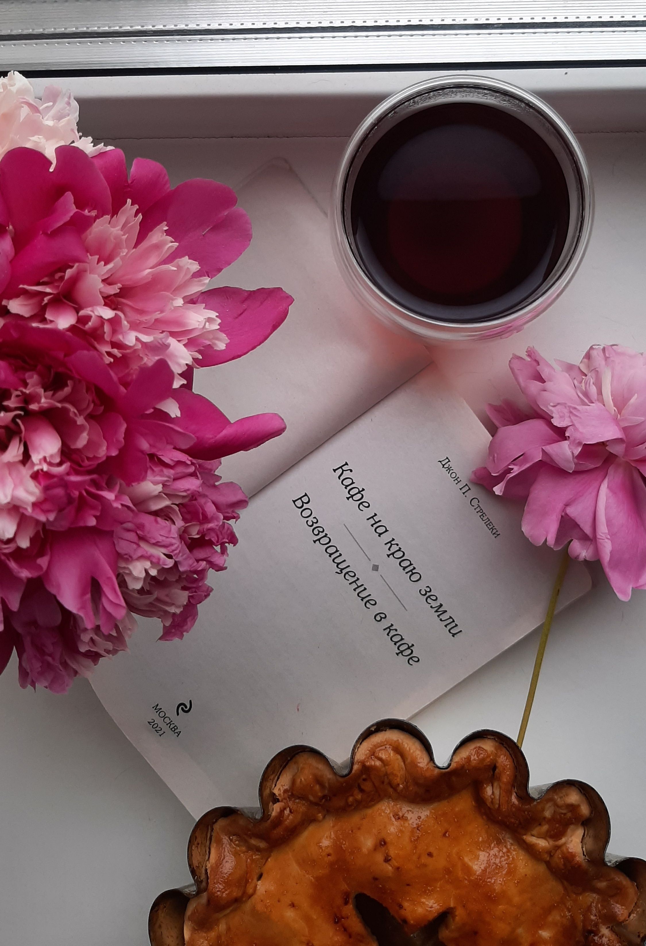 Top view of a cozy tea setup with pink flowers, a beverage, and pastry.