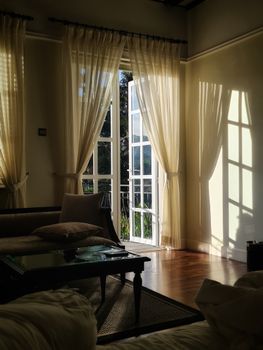 A warm and inviting living room with sunlight streaming through open French doors, casting soft shadows.