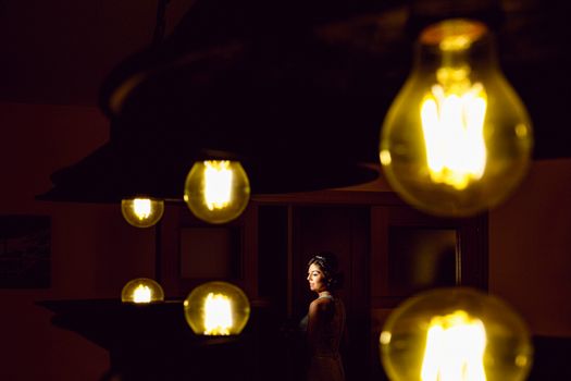 A bride poses elegantly in dramatic lighting surrounded by glowing bulbs, creating a unique wedding portrait.