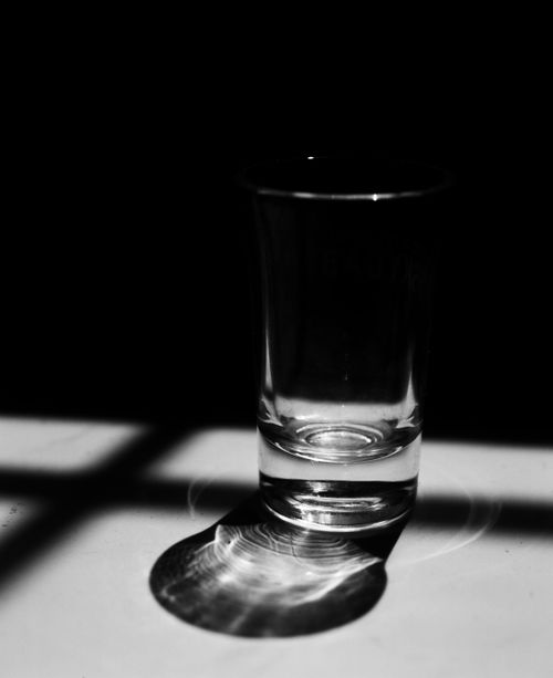 Free Dramatic black and white shot glass with contrasting shadows on a dark background. Stock Photo