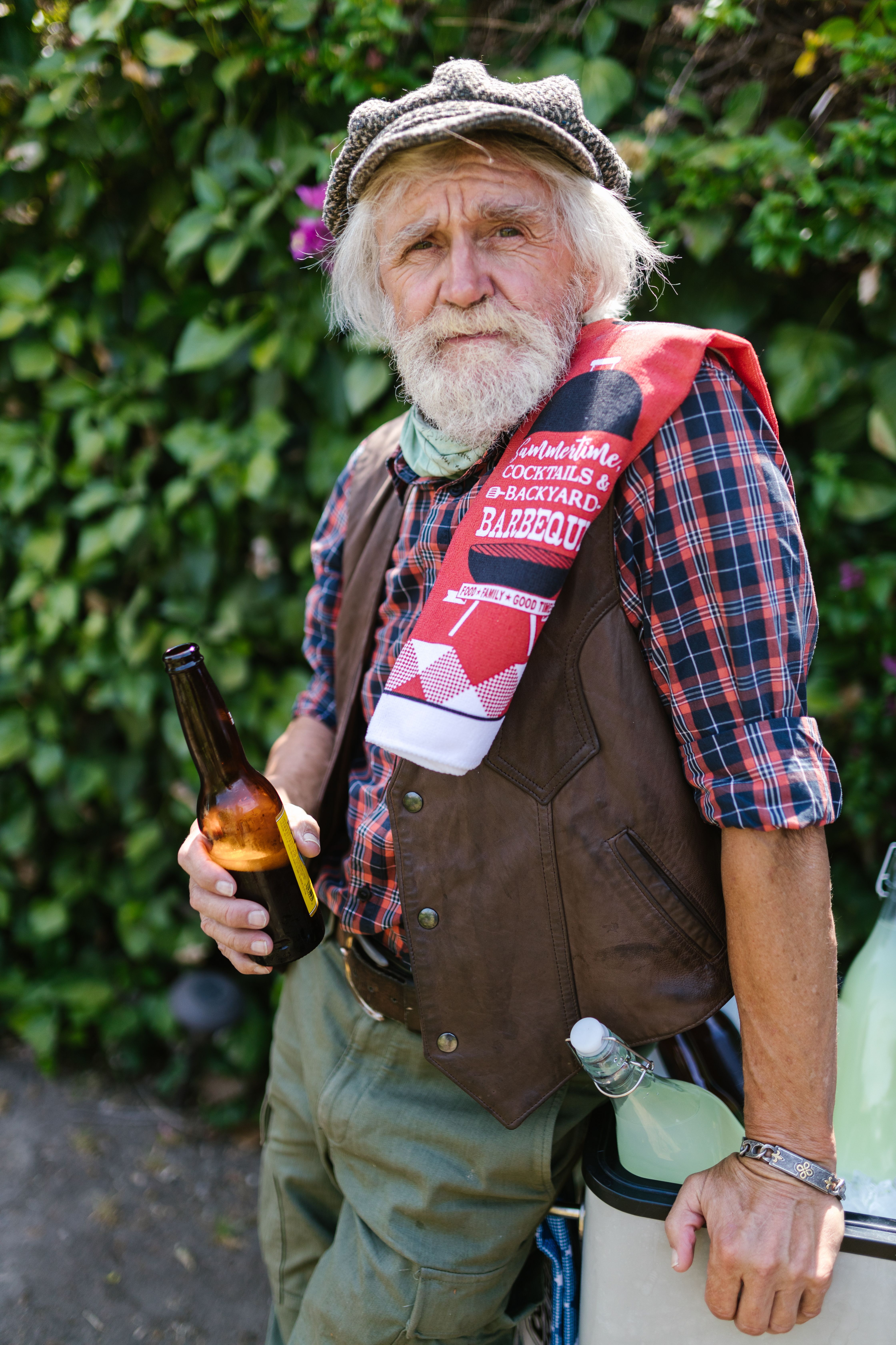 Senior man holding a beer at an outdoor BBQ party, wearing casual attire.