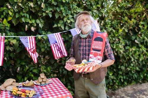 Elderly Man Holding a Tray with Food and Standing in the Garden Decorated for the 4th of July