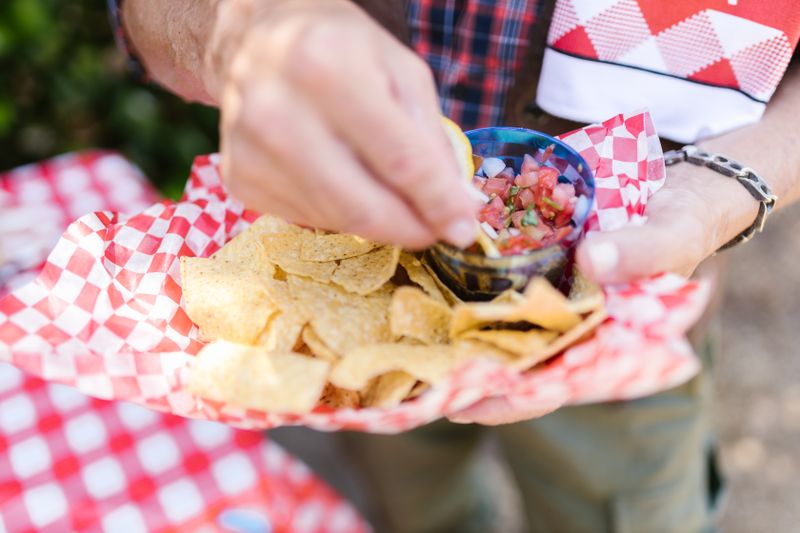 Close-up of a person holding a loaded plate of nachos at an outdoor party