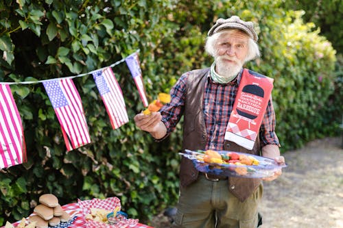 Elderly Man Holding a Tray with Food and Standing in the Garden Decorated for the 4th of July 