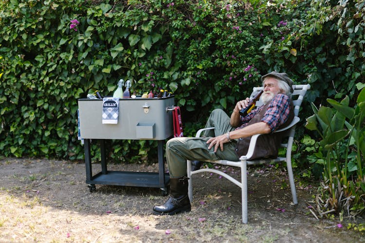 An Elderly Man Holding A Beer While Sitting On A Chair