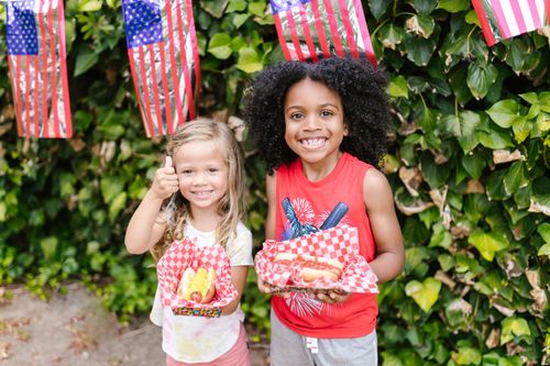 Free Smiling children enjoying hot dogs amidst an outdoor American flag celebration. Stock Photo