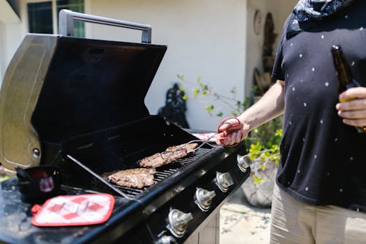 Person grilling steaks on barbecue outdoors, enjoying a sunny day.