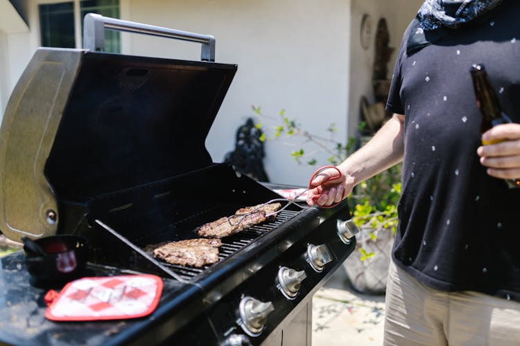 A Person In Black Shirt Cooking Meat While Using Tongs