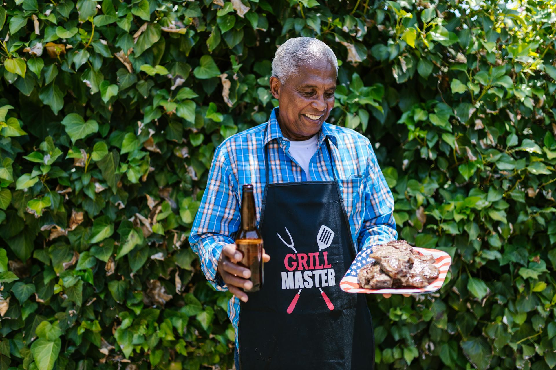 An Elderly man Holding a Plate of Grilled Meat and a Bottle of Beer