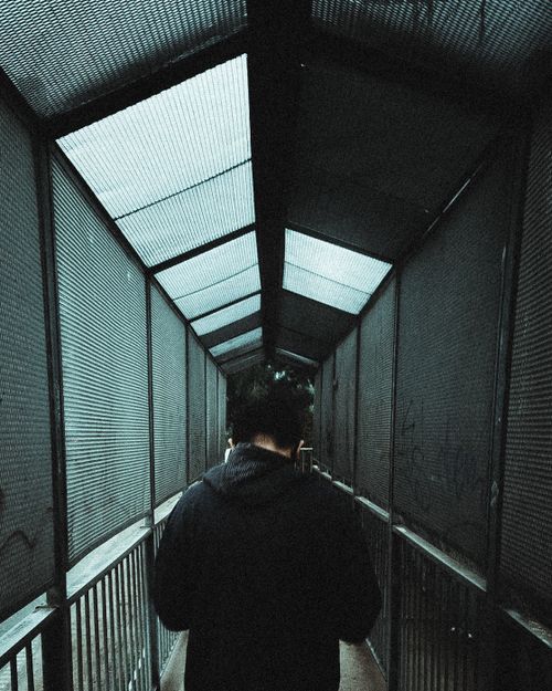 Free Back view of an adult walking through a gritty urban tunnel with metal fencing. Stock Photo