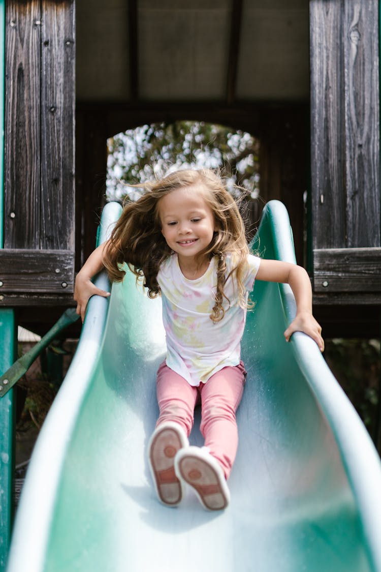 Happy Girl Playing On Slide In The Park