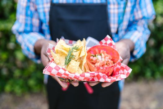 A person holding a basket of nachos with salsa, showcasing delicious outdoor snack options.