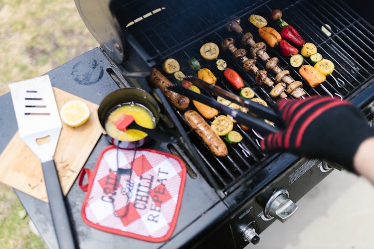 A Person Wearing Black And Red Gloves Grilling Meat