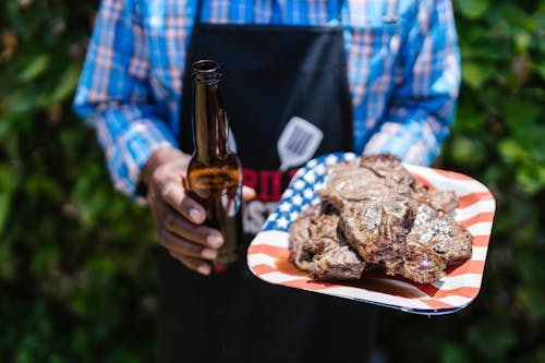Free Person Holding Beer and Grilled Meat on Paper Plate  Stock Photo