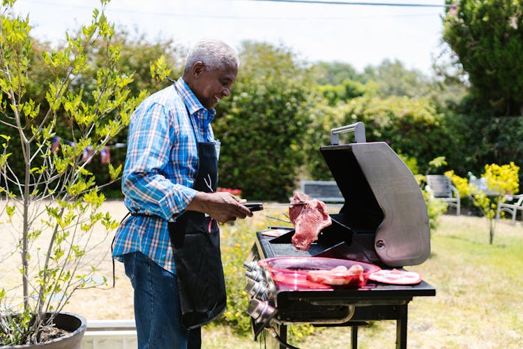 Side View Of A Man Cooking Meat In A Griller