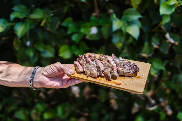 A Person Holding A Sliced Steak On A Wooden Board