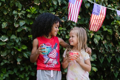 Free Two smiling kids celebrate the 4th of July with American flags outdoors. Stock Photo