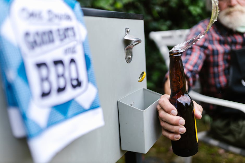 Close-up of a senior man opening a beer bottle at an outdoor barbecue gathering, splashing beer.