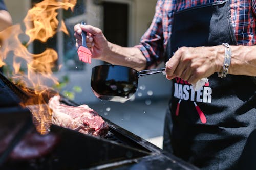 Free Man in Black Apron Putting Sauce on Meat while Grilling Stock Photo