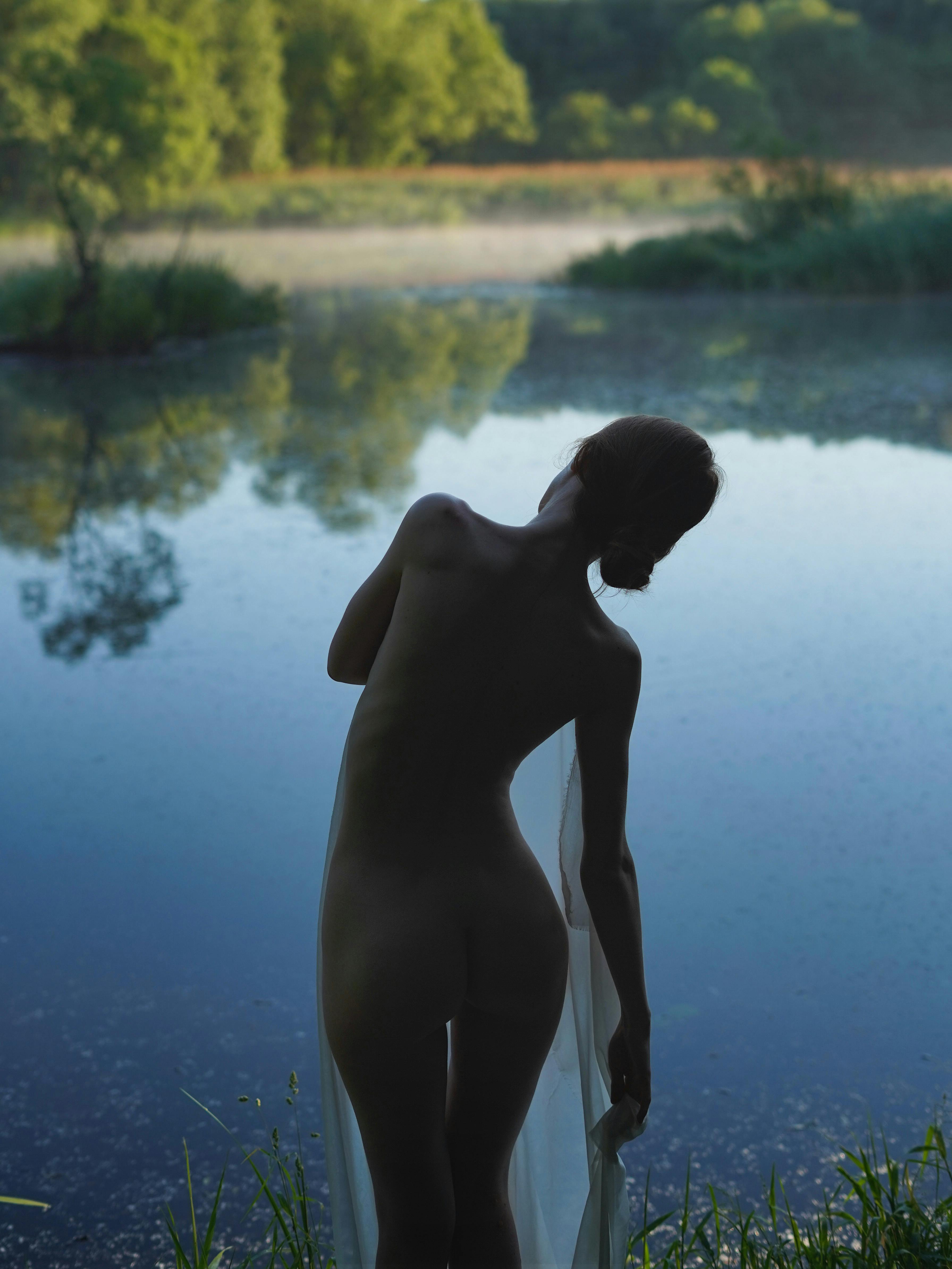 naked woman standing beside a lake
