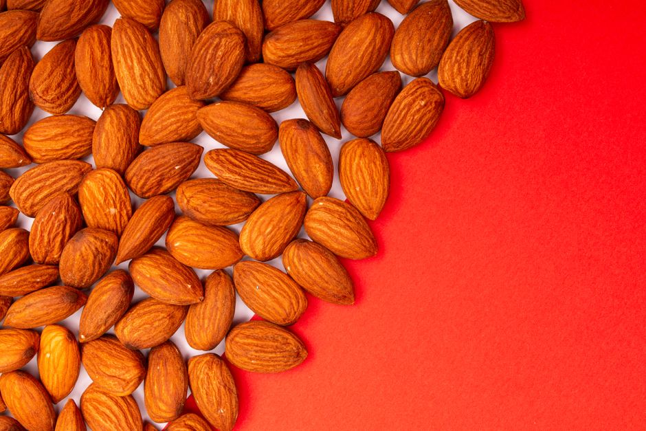High-quality close-up of roasted almonds on a vivid red surface, perfect for food photography. - Where to Buy Quality Dry Fruits in Pakistan
