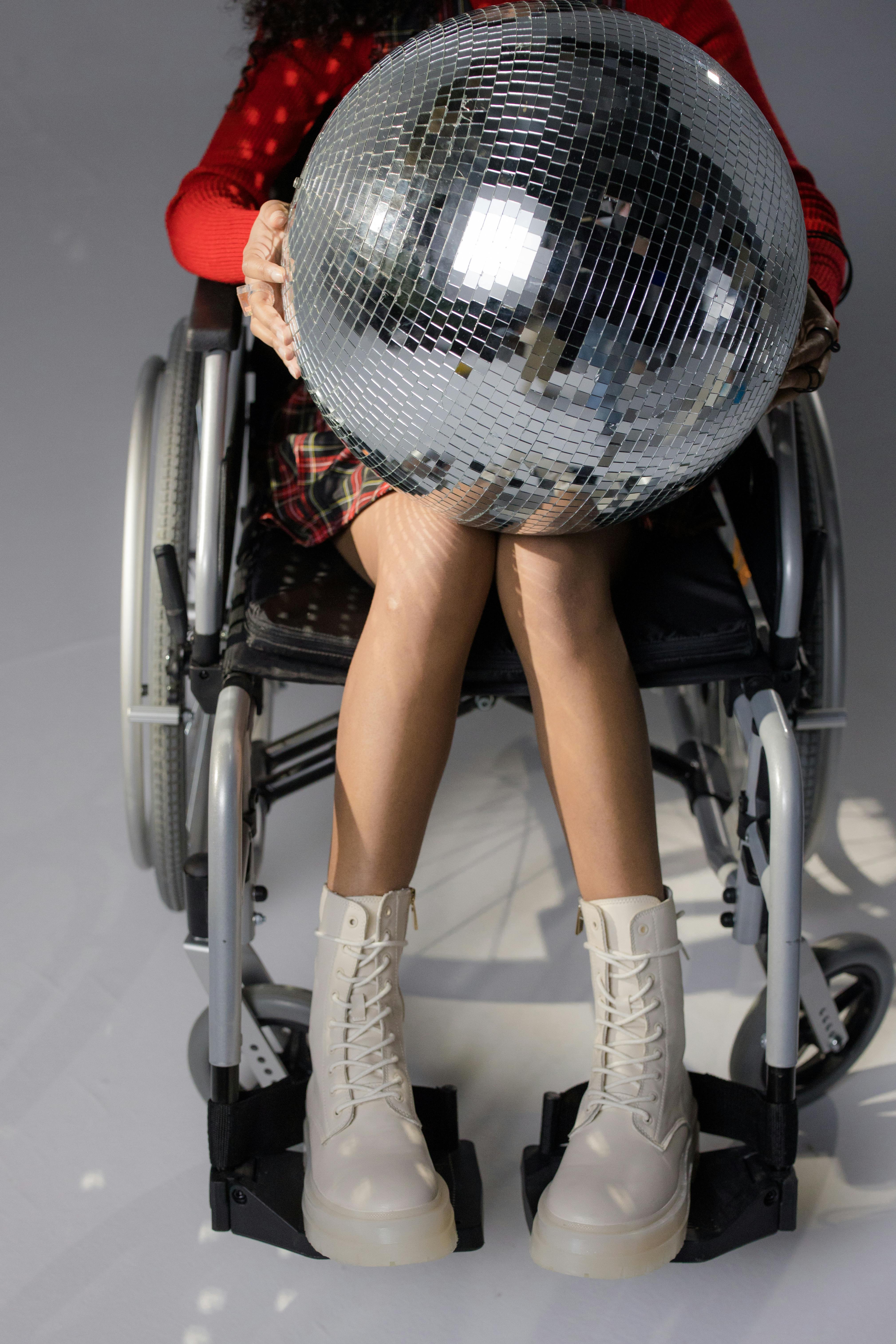 Fashionable woman in wheelchair with disco ball, showing style and inclusivity.