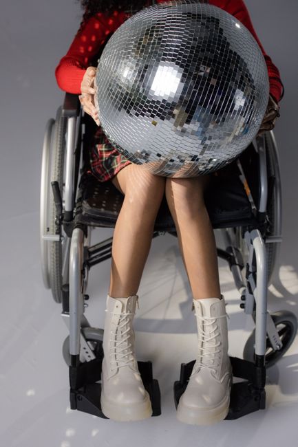 Fashionable woman in wheelchair with disco ball, showing style and inclusivity.
