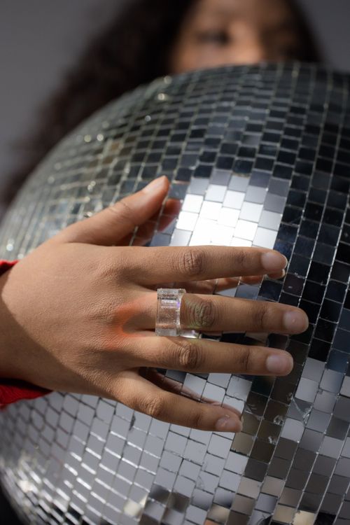Free A close-up shot of a hand with jewelry holding a shiny disco ball reflecting light. Stock Photo