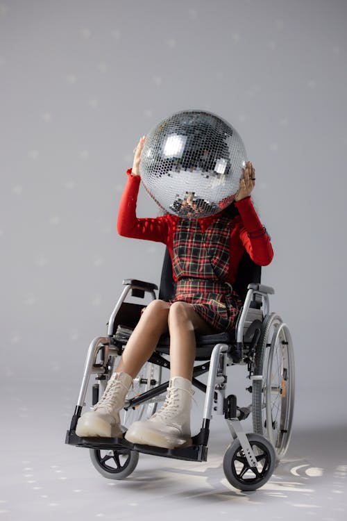 Free Person in red attire sits in wheelchair holding a disco ball. Studio shot. Stock Photo