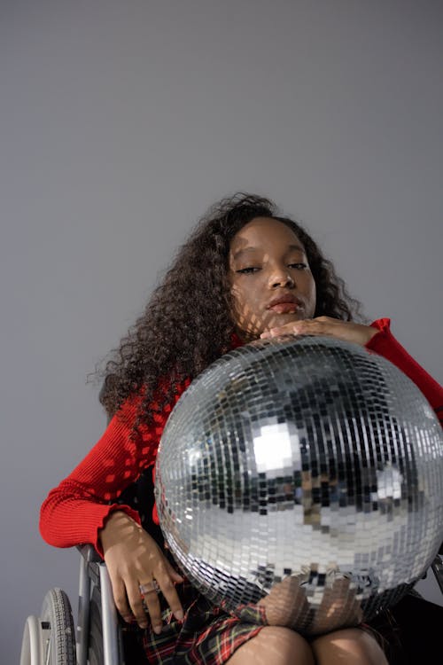 Girl in Red Long Sleeve Shirt Holding Silver  Disco Ball Sitting in Wheelchair